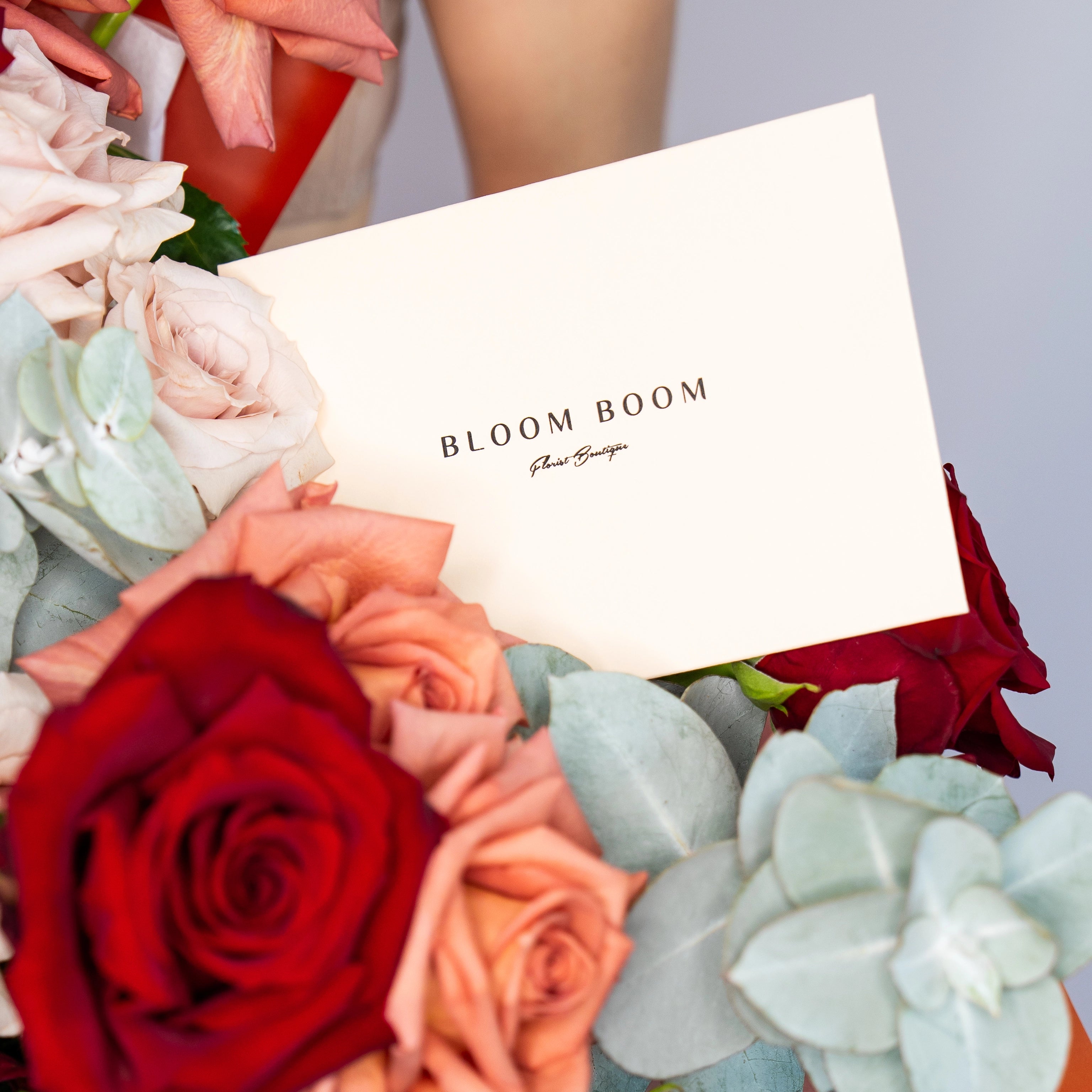 Bloom Boom Floral Boutique white business card nestled in mixed rose bouquet with red, pink and white flowers