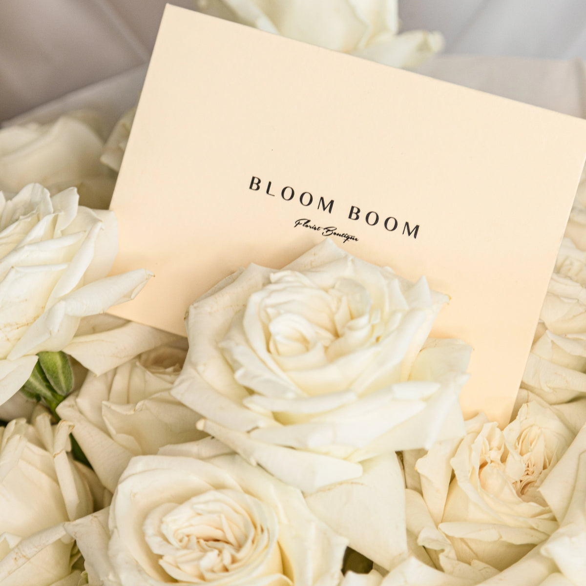 Bloom Boom Floral Boutique business card nestled among ivory white roses with cream colored petals
