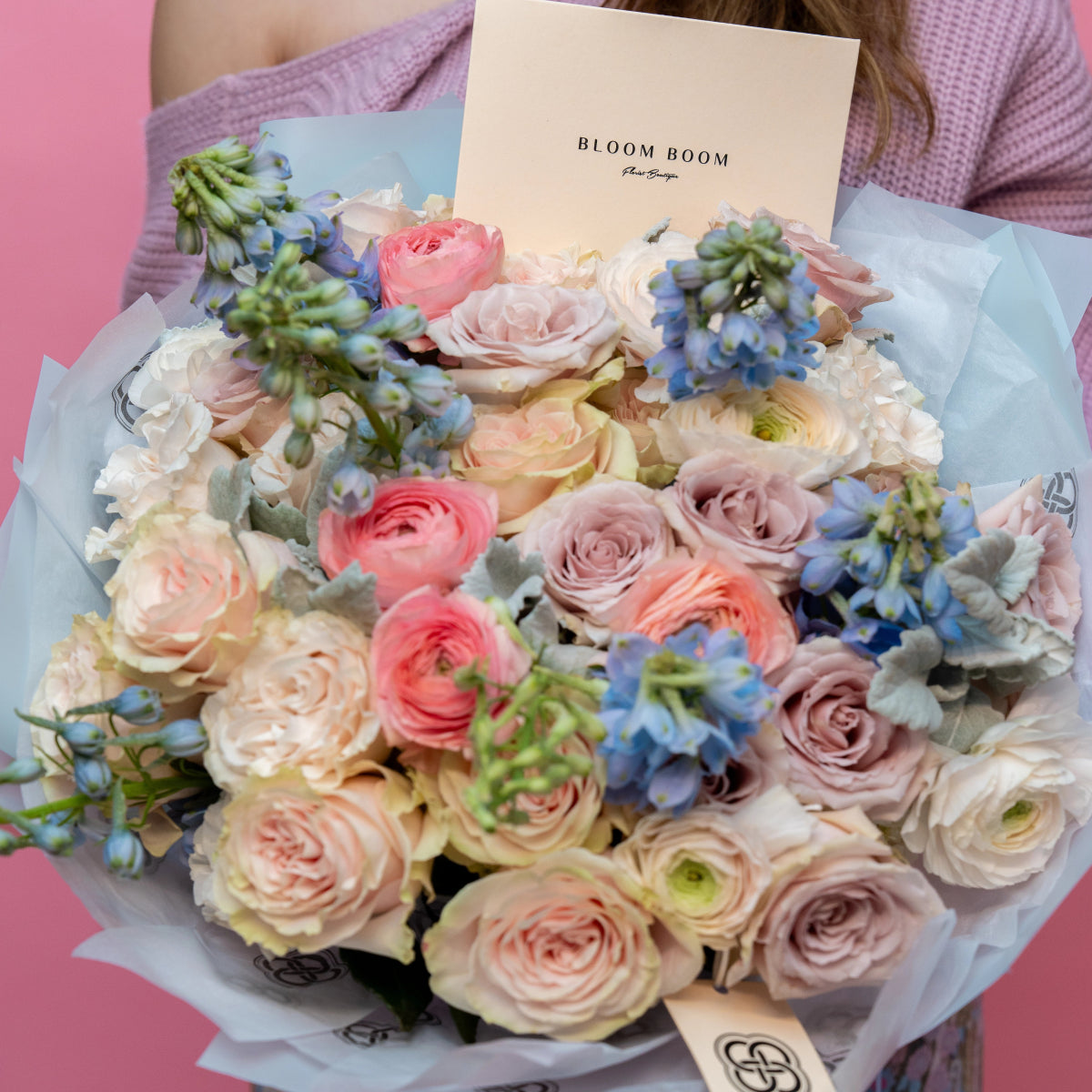 Pastel flower bouquet with pink roses, coral ranunculus, blue delphinium in white tissue paper from Bloom Boom