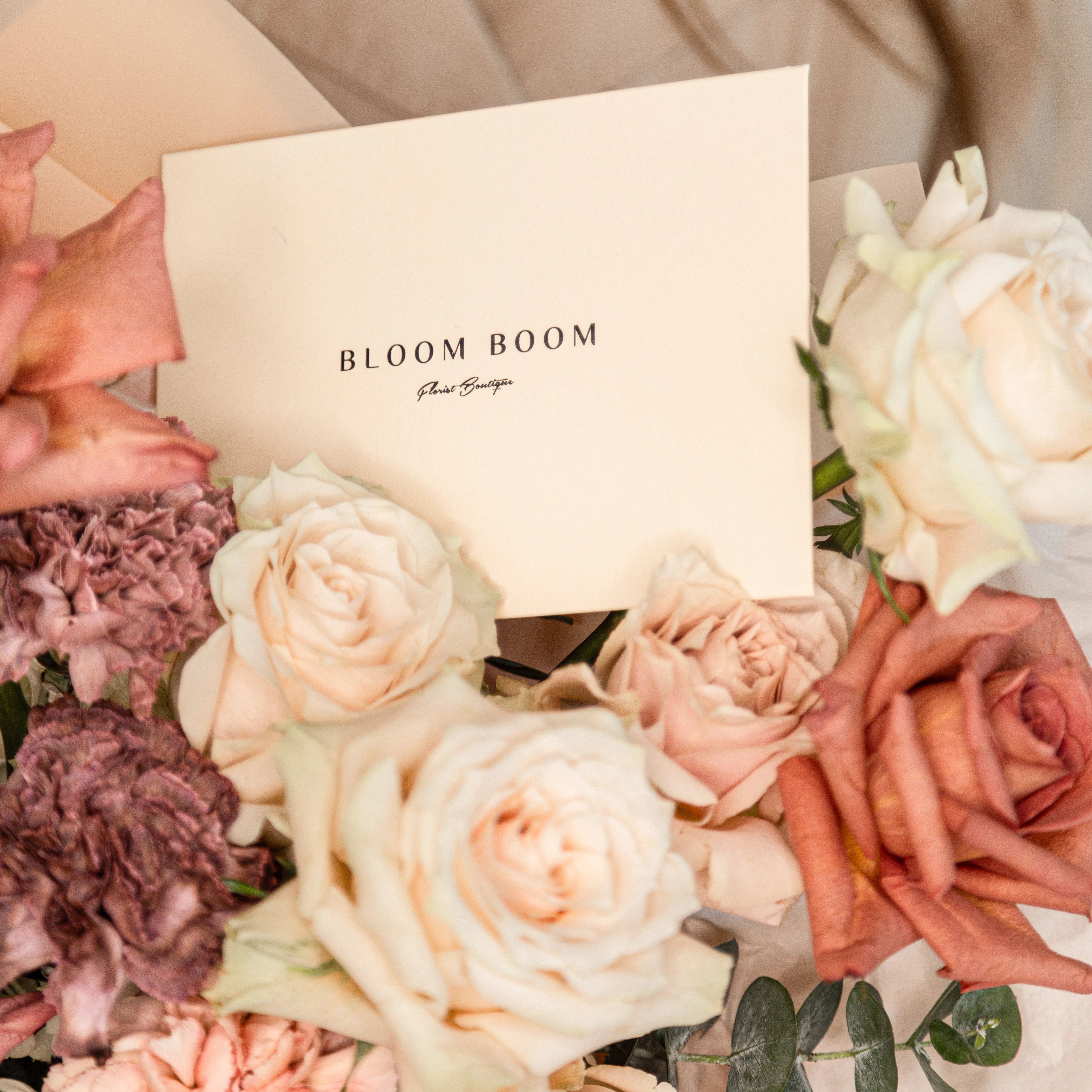 Bloom Boom Flowers logo card with coral roses, cream roses, and mauve chrysanthemums luxury flower arrangement