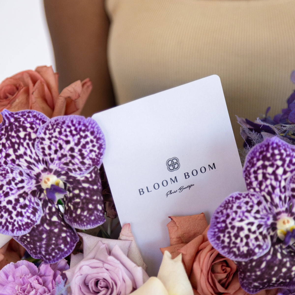 Bloom Boom flower boutique card nestled in mixed floral arrangement with purple spotted orchids and colorful roses