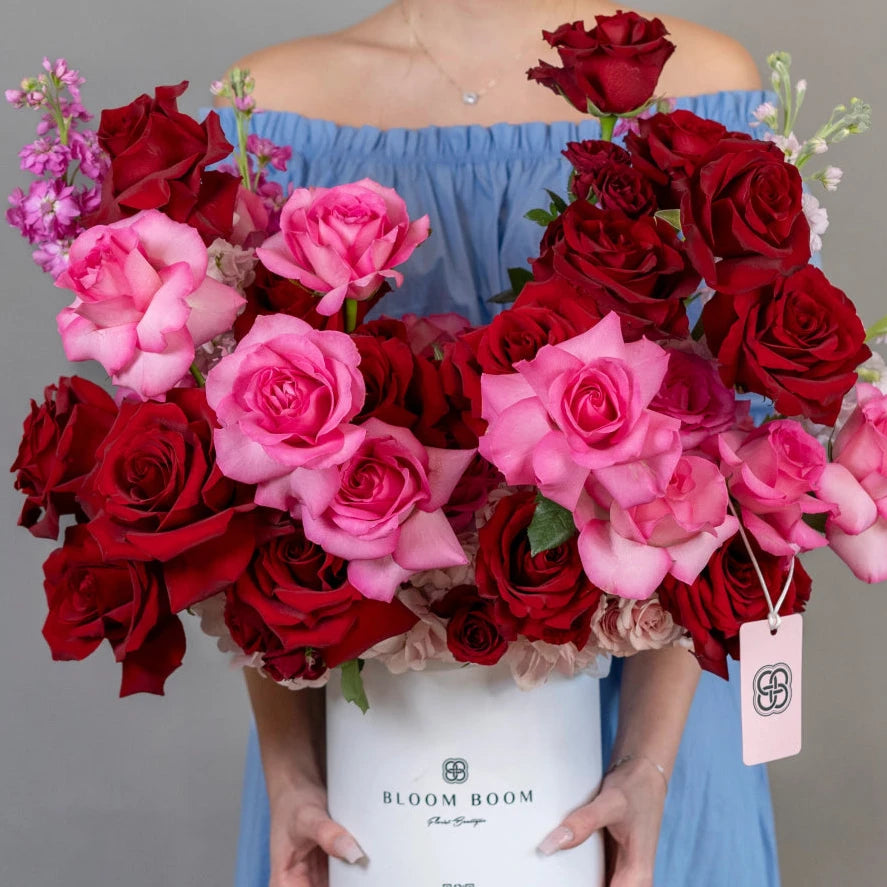 Luxury white flower box with deep red and pink roses, purple stock flowers, woman in blue off-shoulder dress