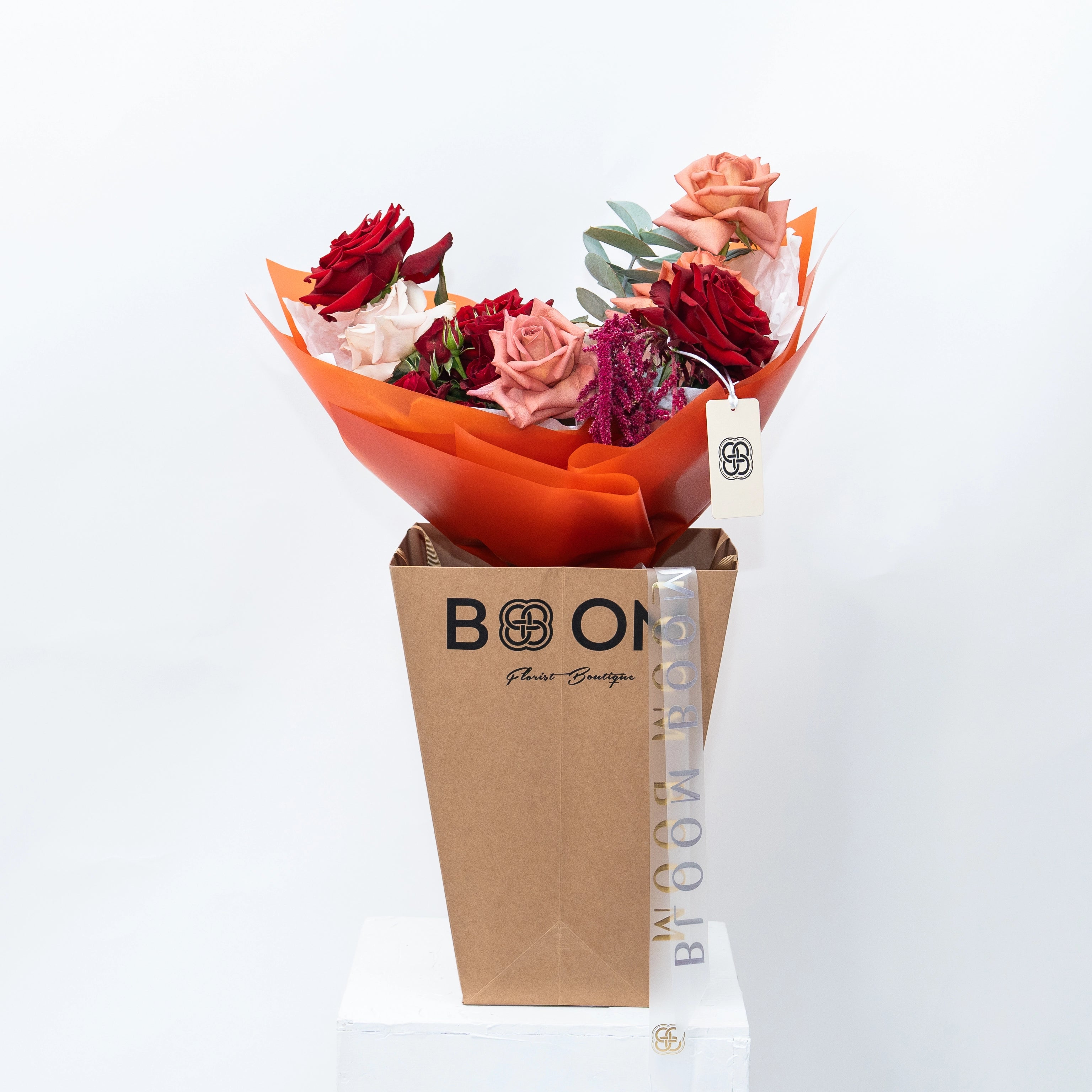 Mixed rose bouquet with red and coral roses in orange paper wrapping, displayed in kraft BLOOM boutique bag