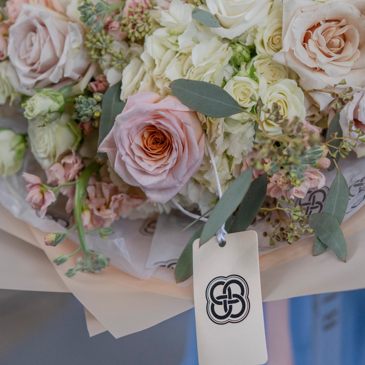 Elegant bridal bouquet with blush pink roses, cream hydrangeas, and eucalyptus leaves with branded tag