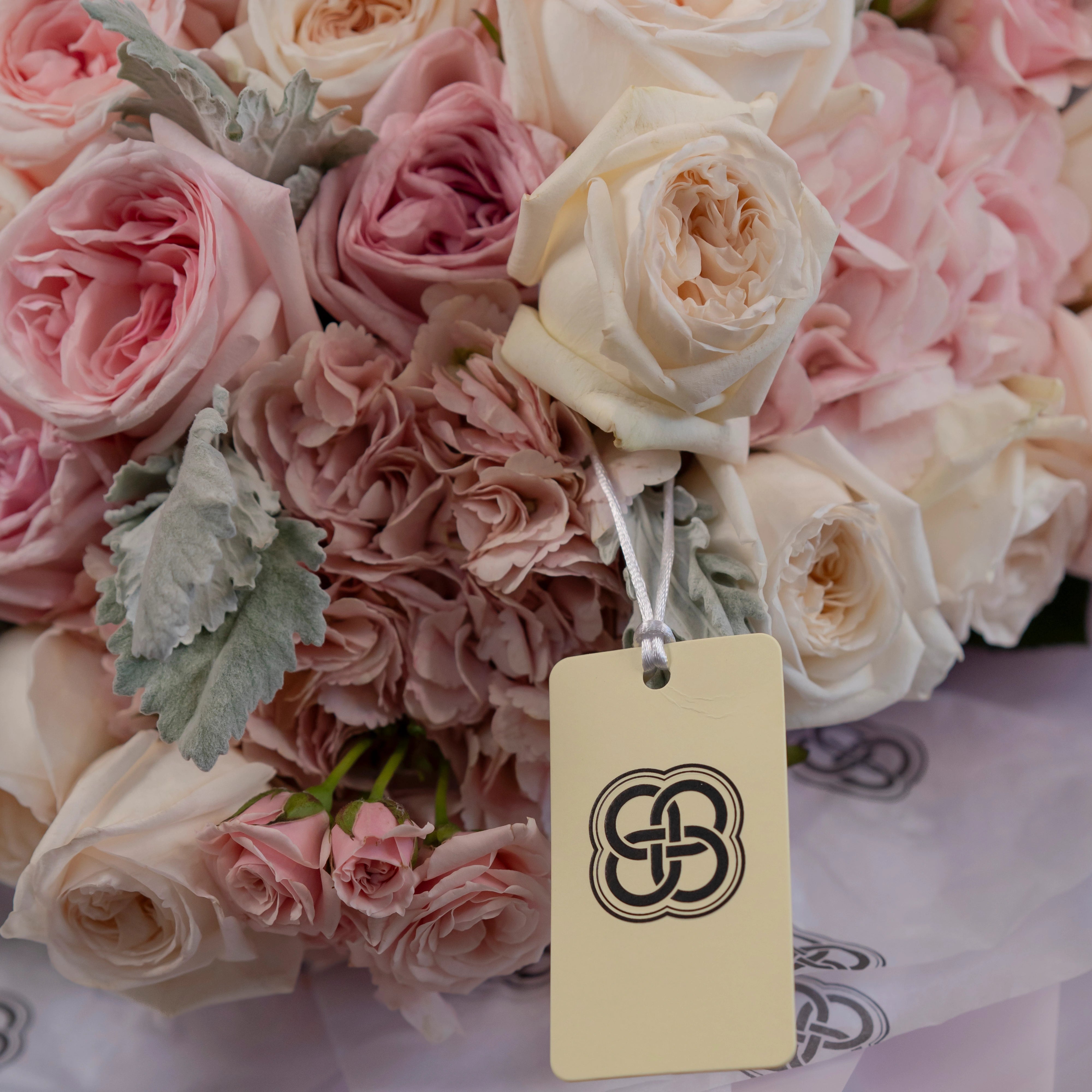 Blush pink and cream garden rose bridal bouquet with dusty miller foliage and elegant gift tag for weddings