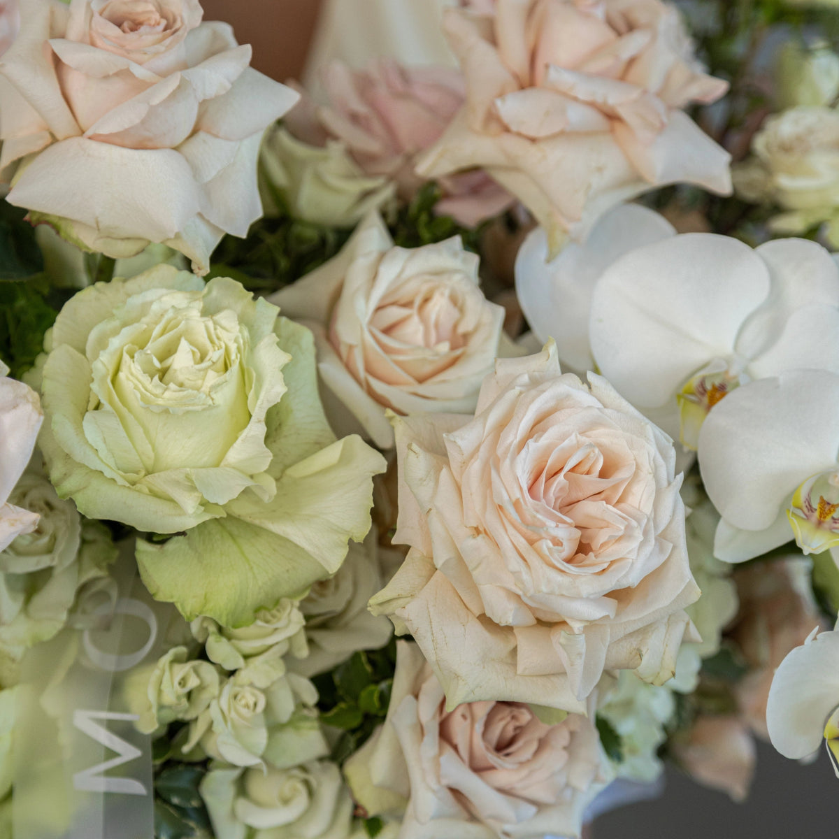 Elegant flower arrangement with blush pink roses, pale green roses, white orchids and small white blooms