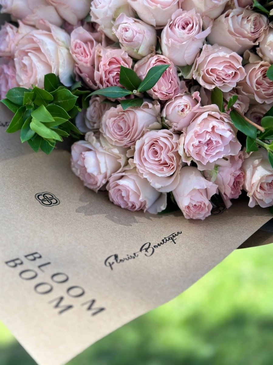 Fresh blush pink roses bouquet with green foliage wrapped in kraft paper for flower delivery