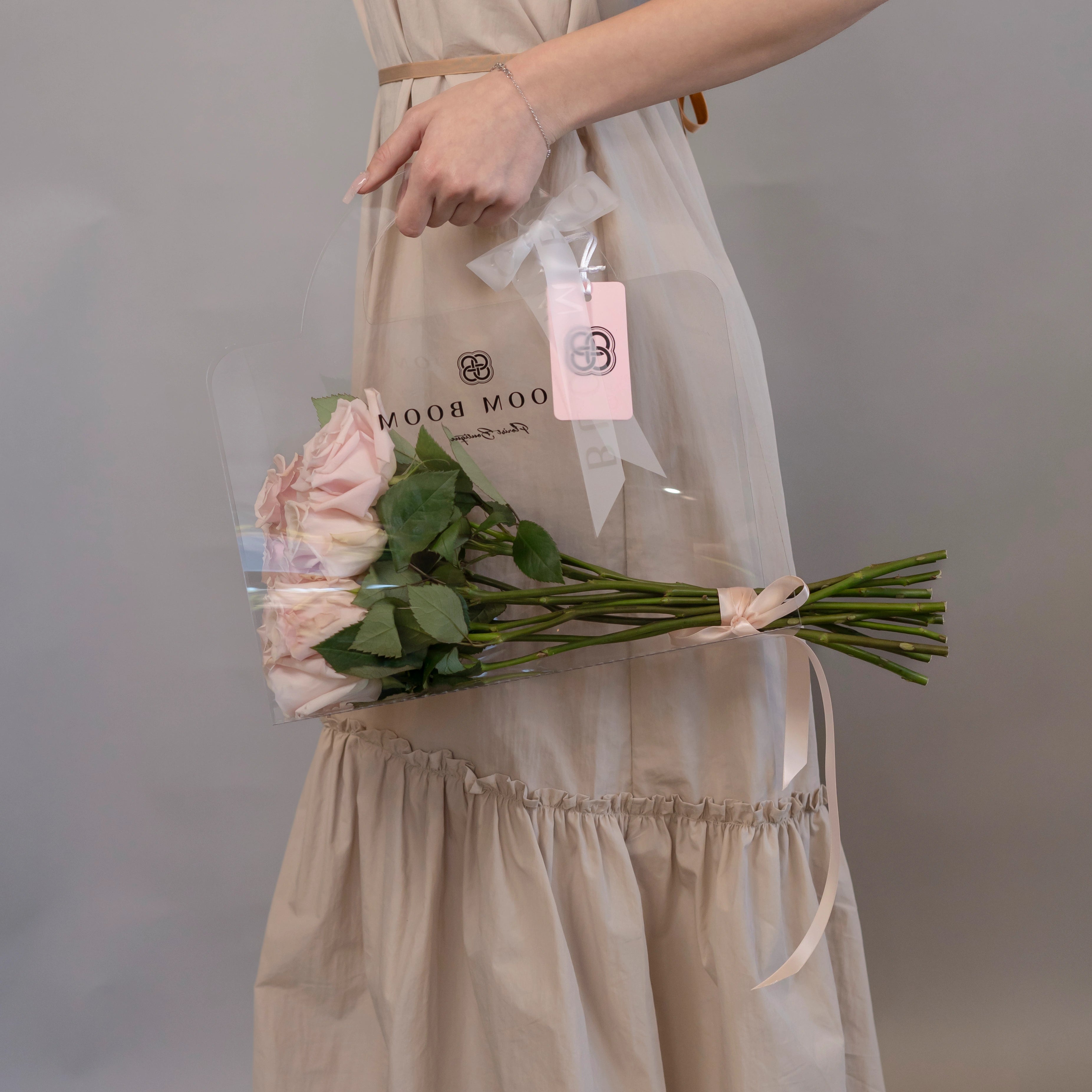 Blush pink long stem roses bouquet with Bloom Boom branded gift bag held by person in beige dress