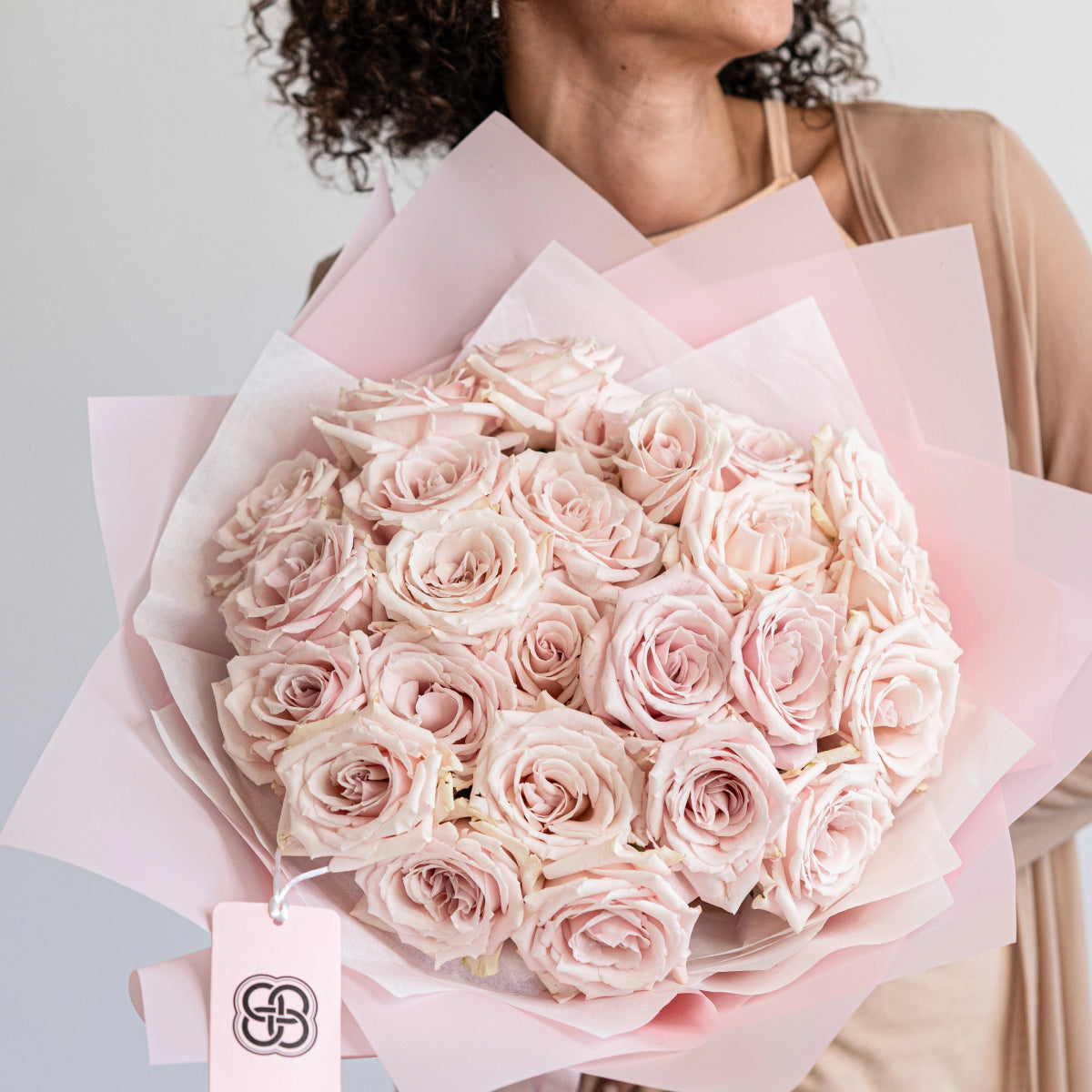 Blush pink rose bouquet with 25 Sweet Escimo roses wrapped in soft pink tissue paper held by woman