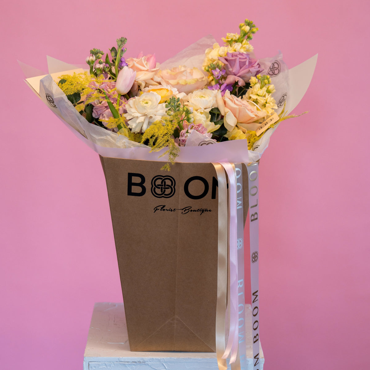 Mixed flower bouquet with pink roses, white tulips, yellow mimosa in brown BOOM Florist Boutique paper bag