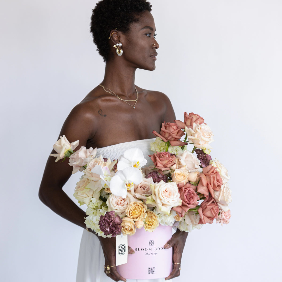 Pink velvet flower box with coral roses, white orchids, and mixed blooms held by woman in white strapless dress