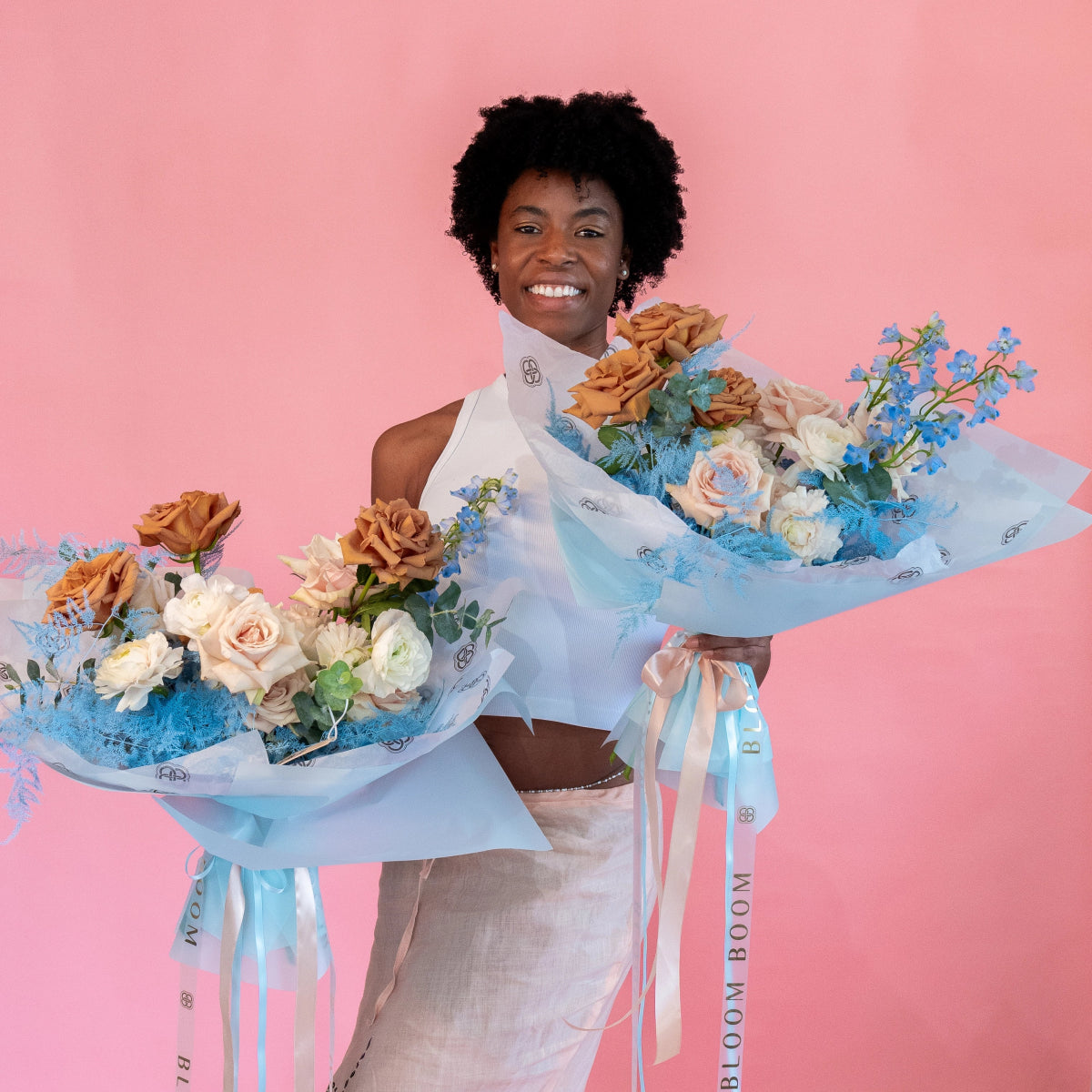 Woman holding two floral bouquets with orange roses, white flowers and blue delphinium in light blue wrapping