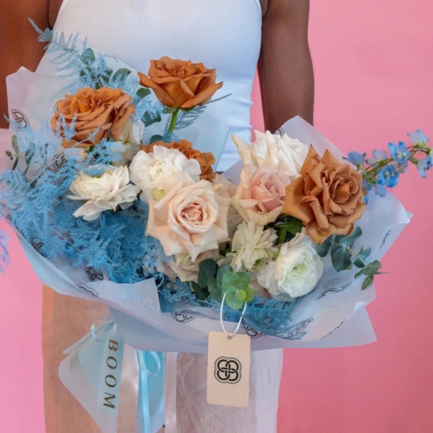 Mixed flower bouquet with peach roses, white ranunculus, and blue accents wrapped in clear cellophane