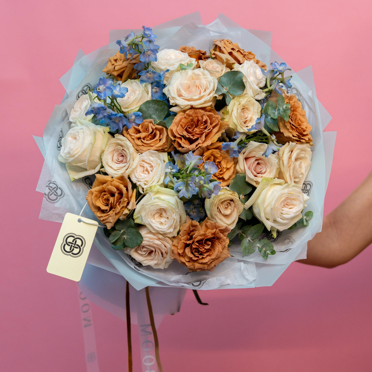 Cappuccino bouquet with cream and bronze roses, blue delphinium flowers, eucalyptus leaves in clear wrap