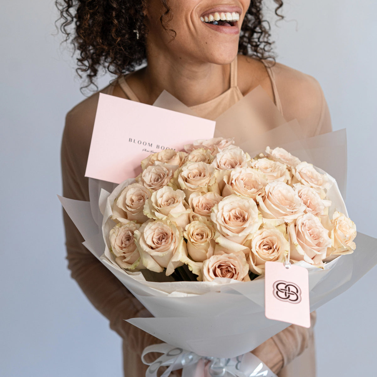Champagne quicksand roses bouquet in white paper wrapping with pink Bloom Boom card and brand tag