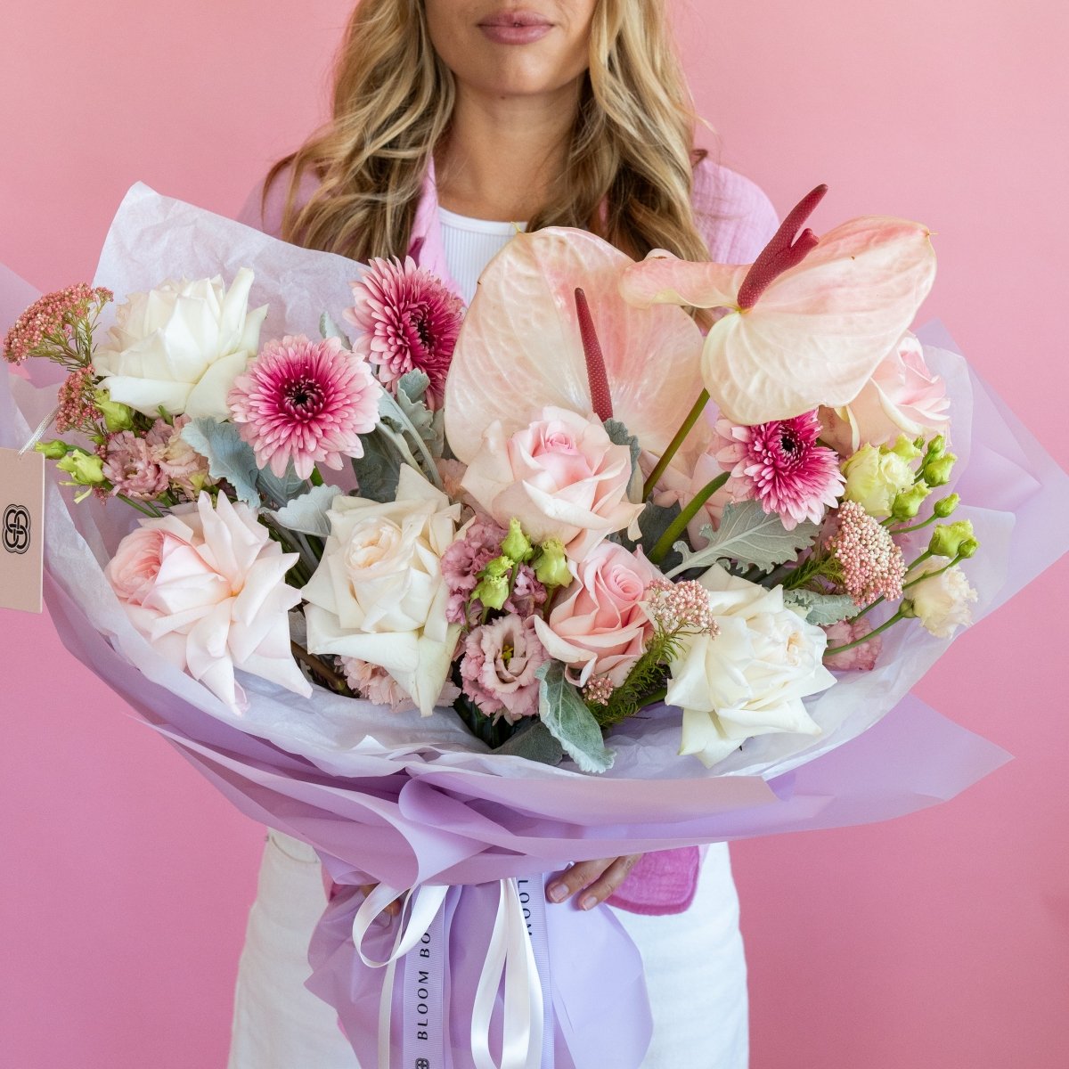Mixed flower bouquet with pink anthurium, white roses, pink chrysanthemums wrapped in lavender paper with ribbon