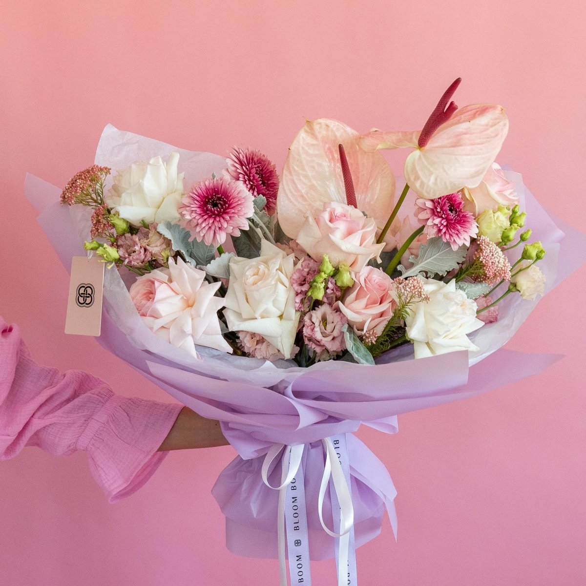 Pink and white mixed flower bouquet with anthurium, roses, chrysanthemums wrapped in lavender paper with ribbon