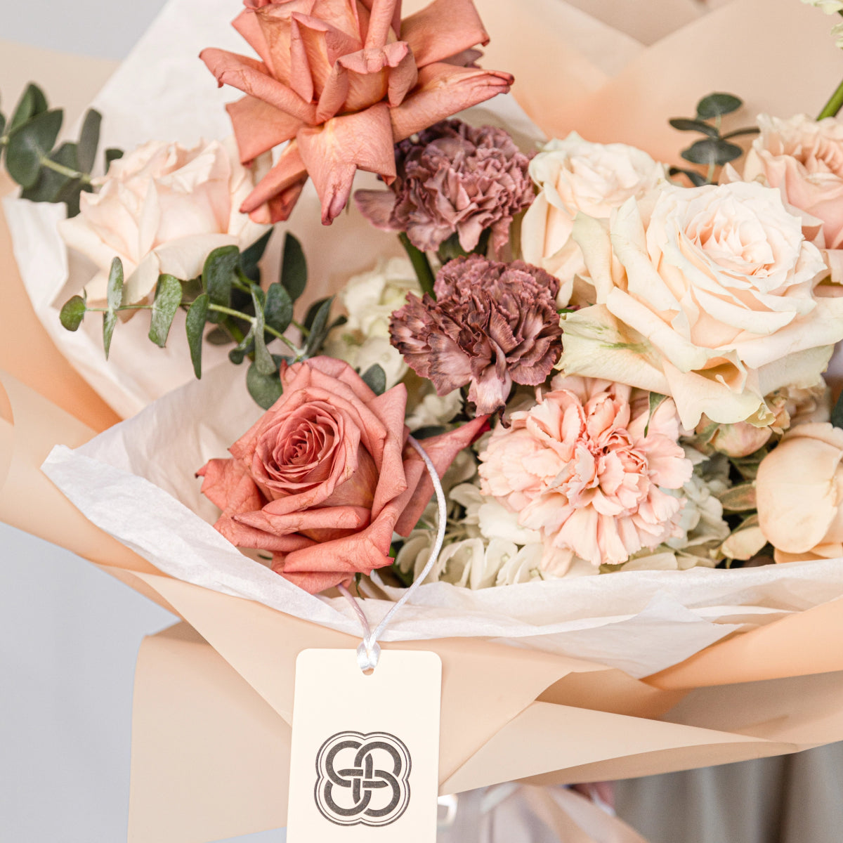 Elegant mixed flower bouquet with coral roses, burgundy carnations, white hydrangea and eucalyptus in kraft paper