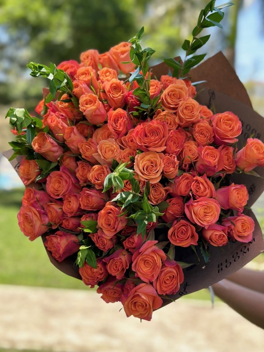 Large coral orange rose bouquet with green foliage wrapped in brown paper for delivery or gift giving