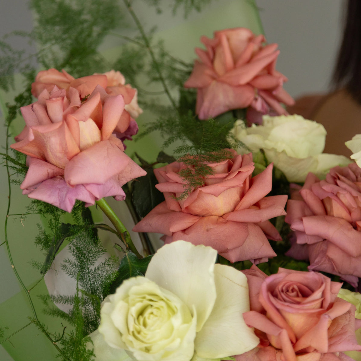 Mixed rose bouquet with coral pink and cream white roses accented by delicate green fern foliage