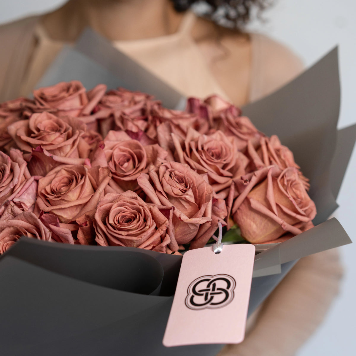 Dusty pink rose bouquet wrapped in gray paper with brand tag, premium fresh flowers for special occasions