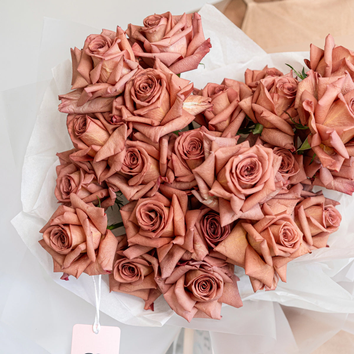 Dusty rose pink roses bouquet wrapped in white paper with gift tag, premium fresh flowers arrangement