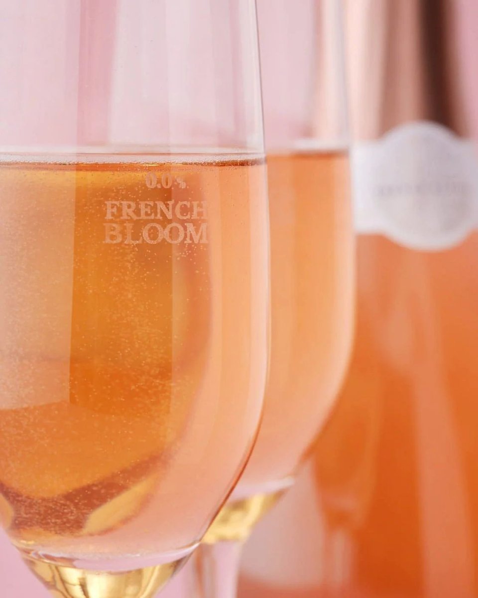 Two glasses of golden-orange sparkling French Bloom non-alcoholic rosé with elegant etched branding on pink background