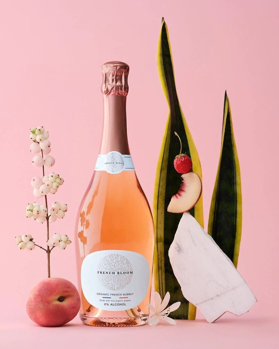 French Bloom rosé sparkling wine bottle with pink foil, white label on pink background with peach and flowers