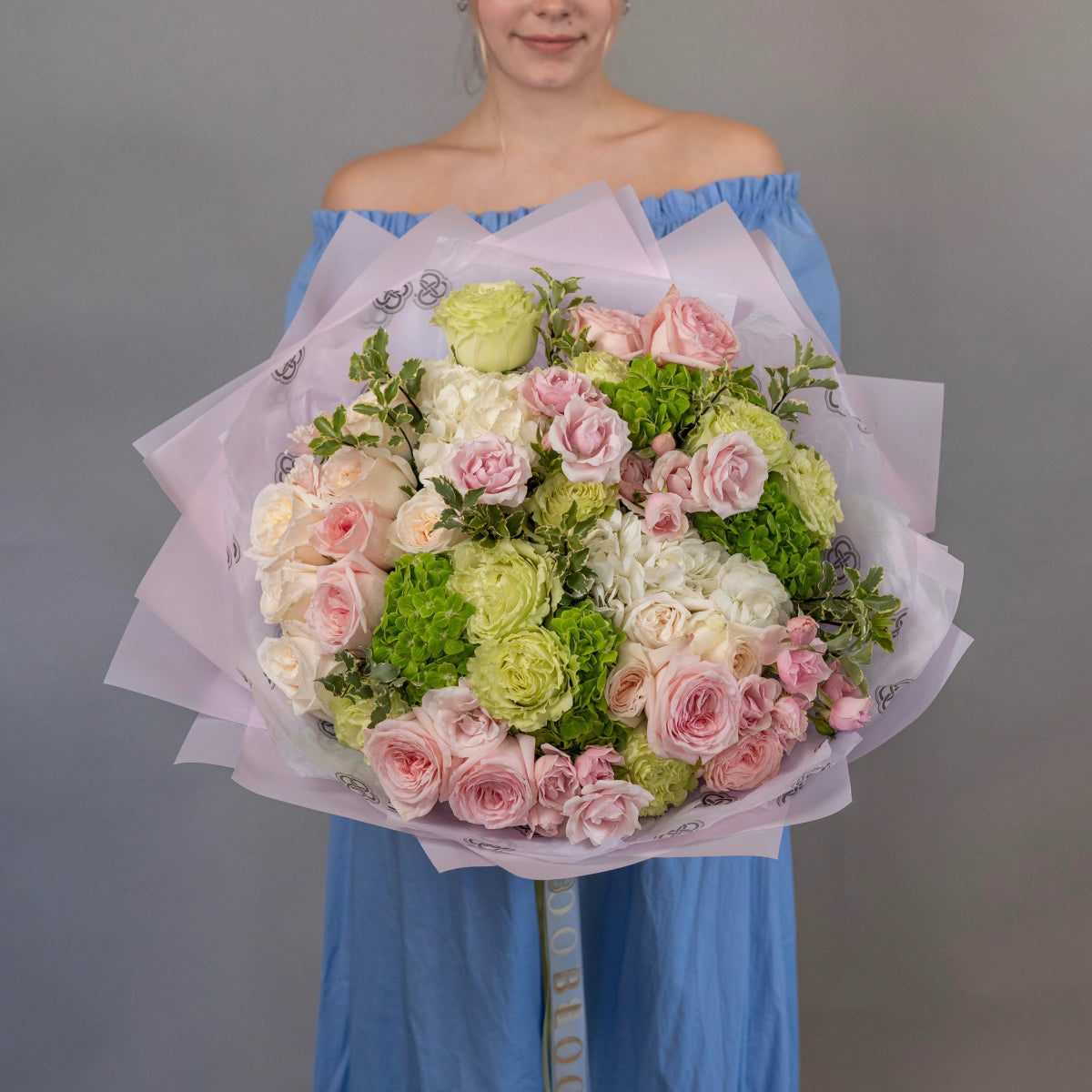 Mixed flower bouquet with pink roses, white hydrangea, and green carnations wrapped in purple tissue paper