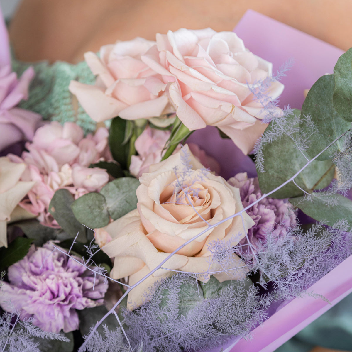 Pastel flower bouquet with blush roses, purple carnations, eucalyptus and lavender dusty miller in lilac wrap