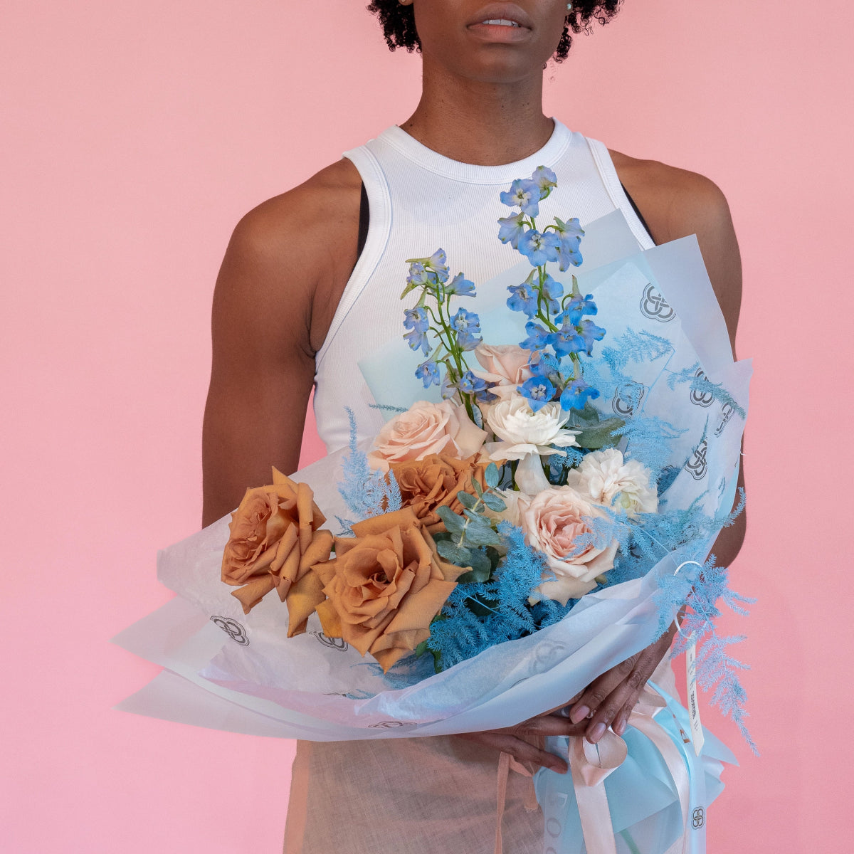 Mixed flower bouquet with peach roses, blue delphinium, and white flowers wrapped in blue tissue paper