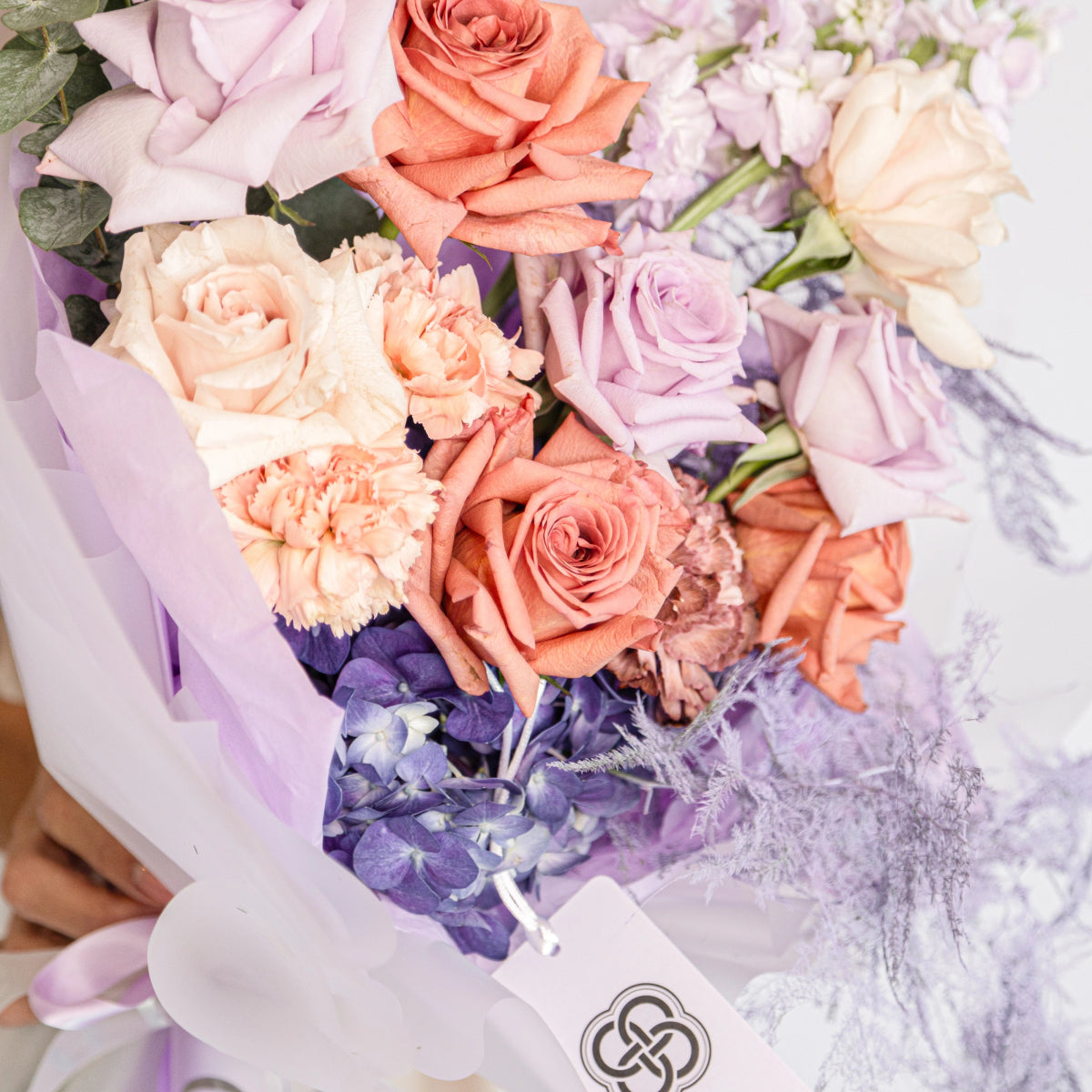 Mixed flower bouquet with coral roses, purple hydrangea, peach carnations wrapped in lavender paper with ribbon