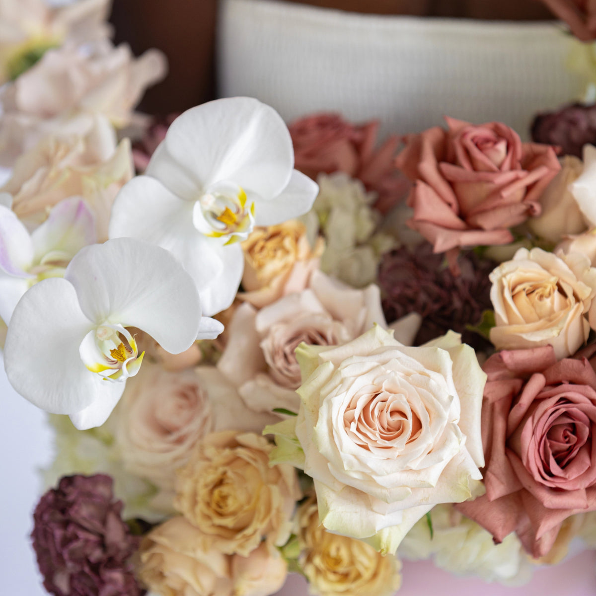 Mixed flower arrangement with white orchids, peach roses, coral roses, and purple blooms in neutral tones