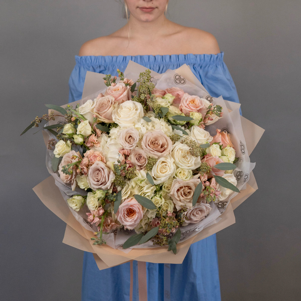 Large mixed rose bouquet with blush pink, cream and white roses wrapped in kraft paper held by woman in blue dress