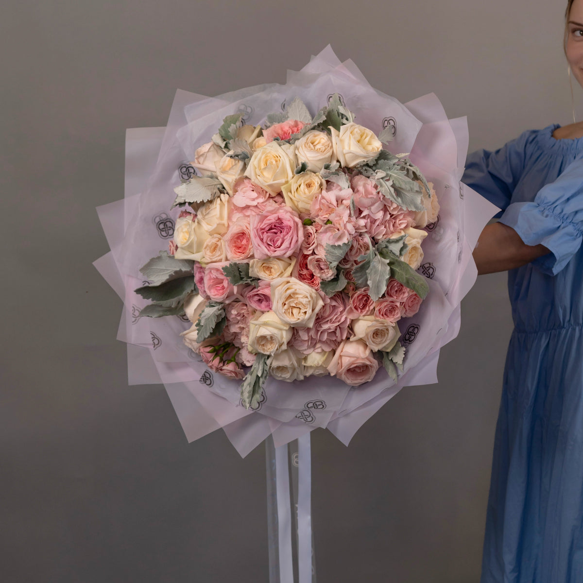 Large mixed rose bouquet in cream, pink and coral tones wrapped in lavender tissue paper with decorative pattern