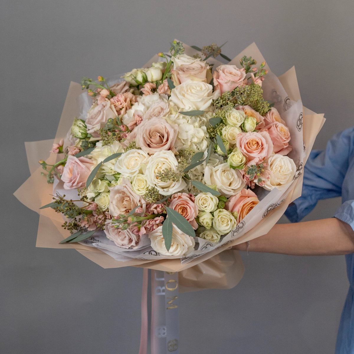 Elegant mixed rose bouquet with cream, pink and peach roses, white hydrangeas and greenery in kraft paper wrapping