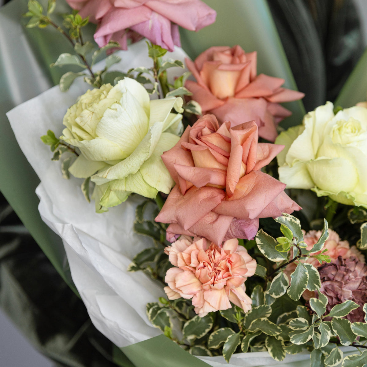 Mixed flower bouquet with white and coral roses, pink carnations, and green foliage wrapped in white paper