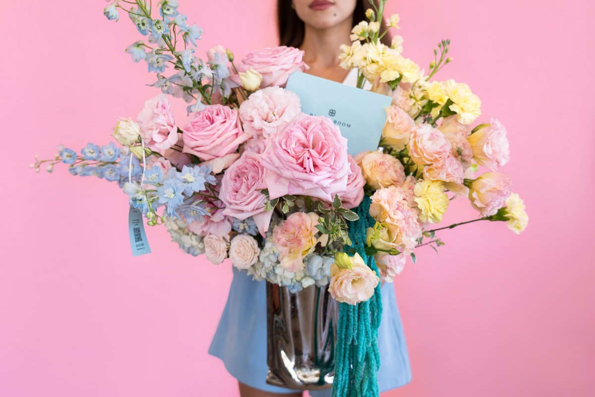 Mixed spring bouquet with pink roses, blue delphinium, yellow carnations in clear glass vase with teal ribbon