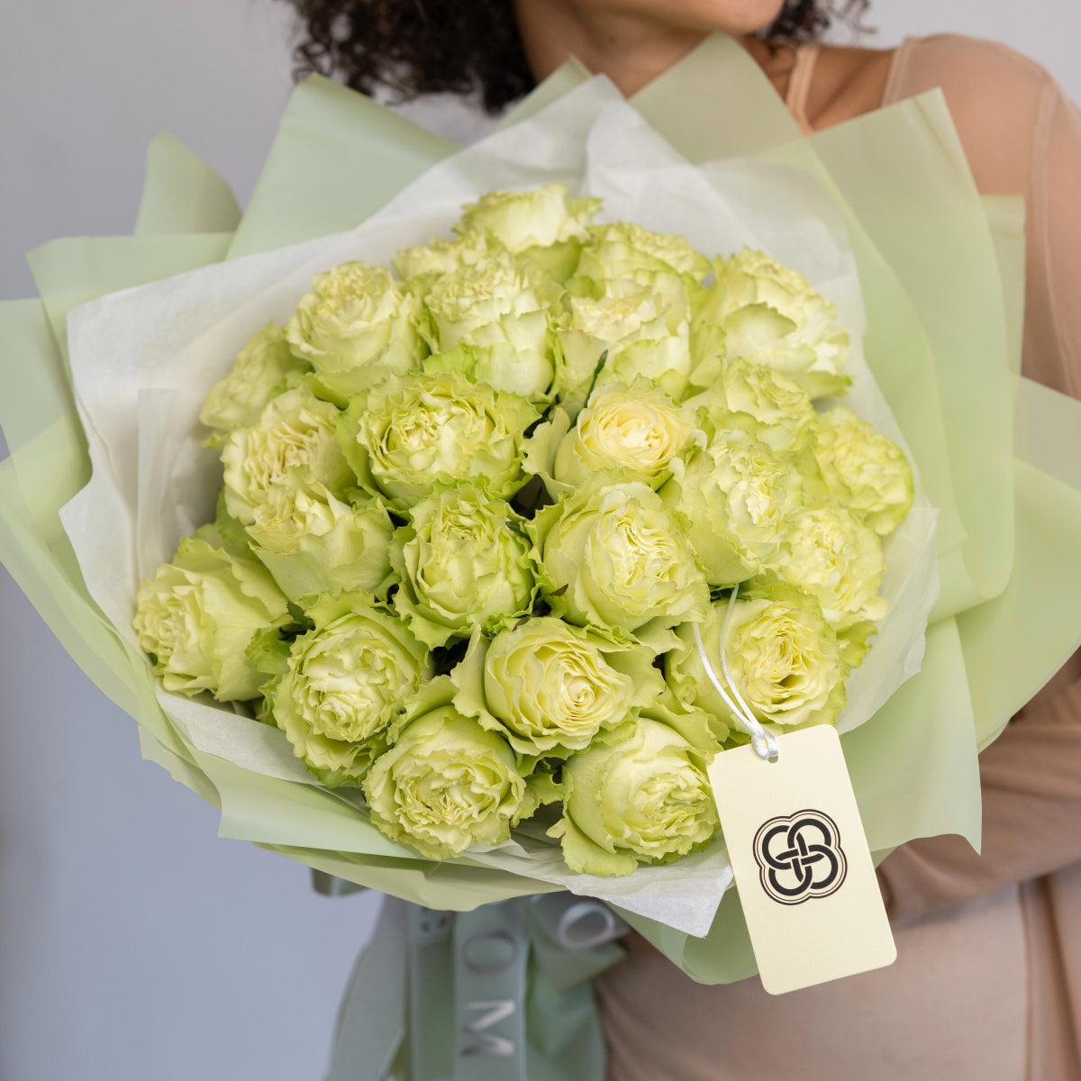 Fresh pale green roses bouquet wrapped in sage green paper with white tissue and branded tag