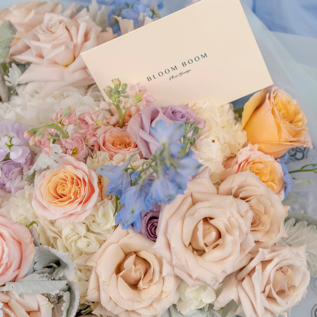 Pastel bridal bouquet with peach roses, lavender flowers, white ranunculus and Bloom Boom florist card