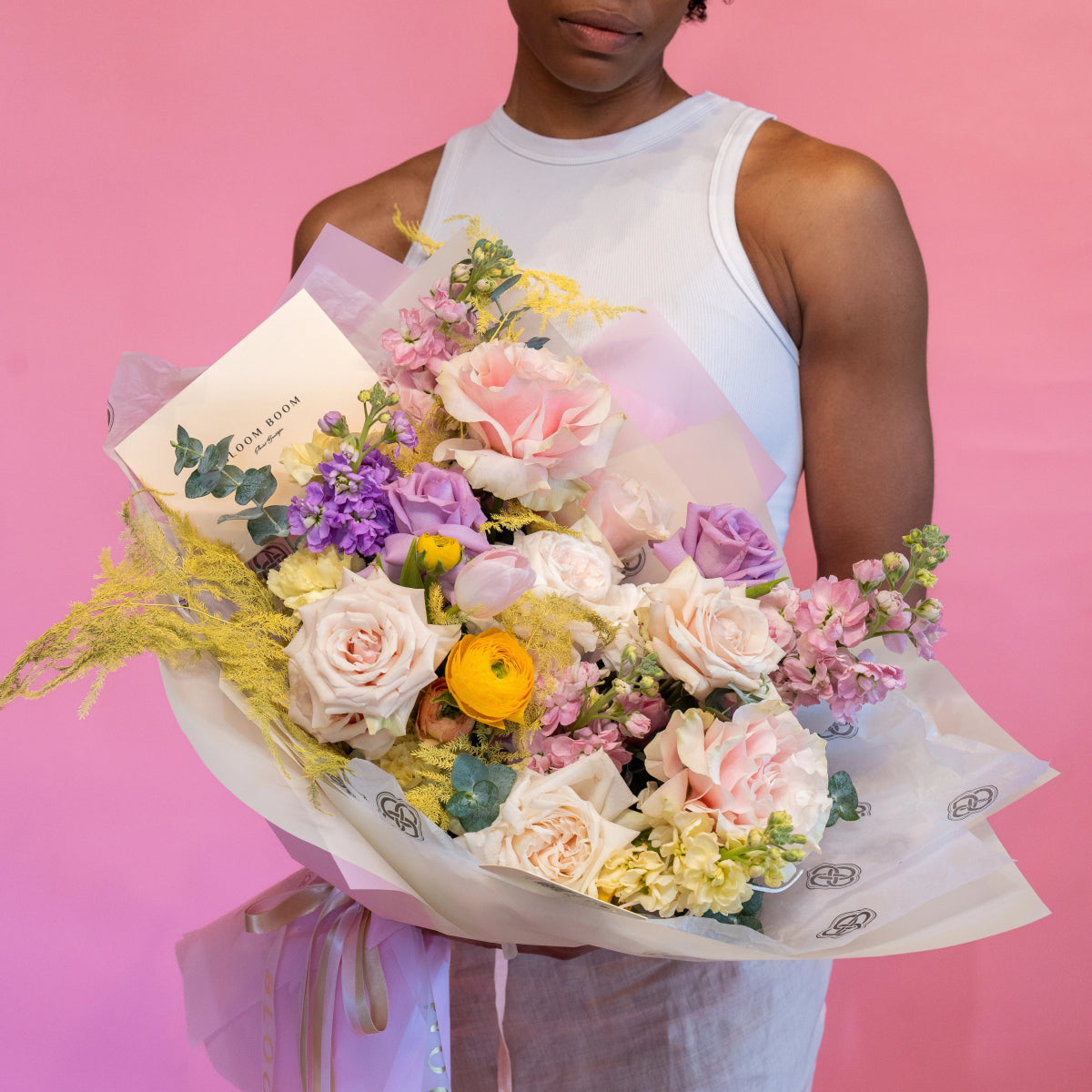 Pastel mixed flower bouquet with pink roses, purple flowers, yellow ranunculus and golden foliage in white paper