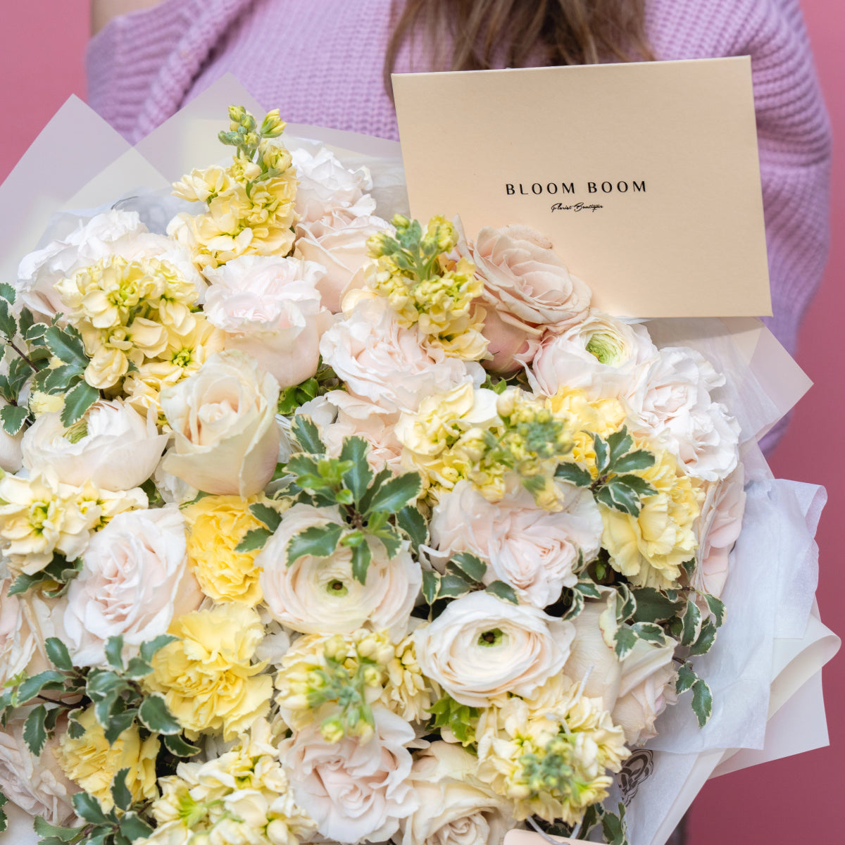 Pastel yellow and blush pink flower bouquet with roses, ranunculus and greenery in white tissue paper wrapping