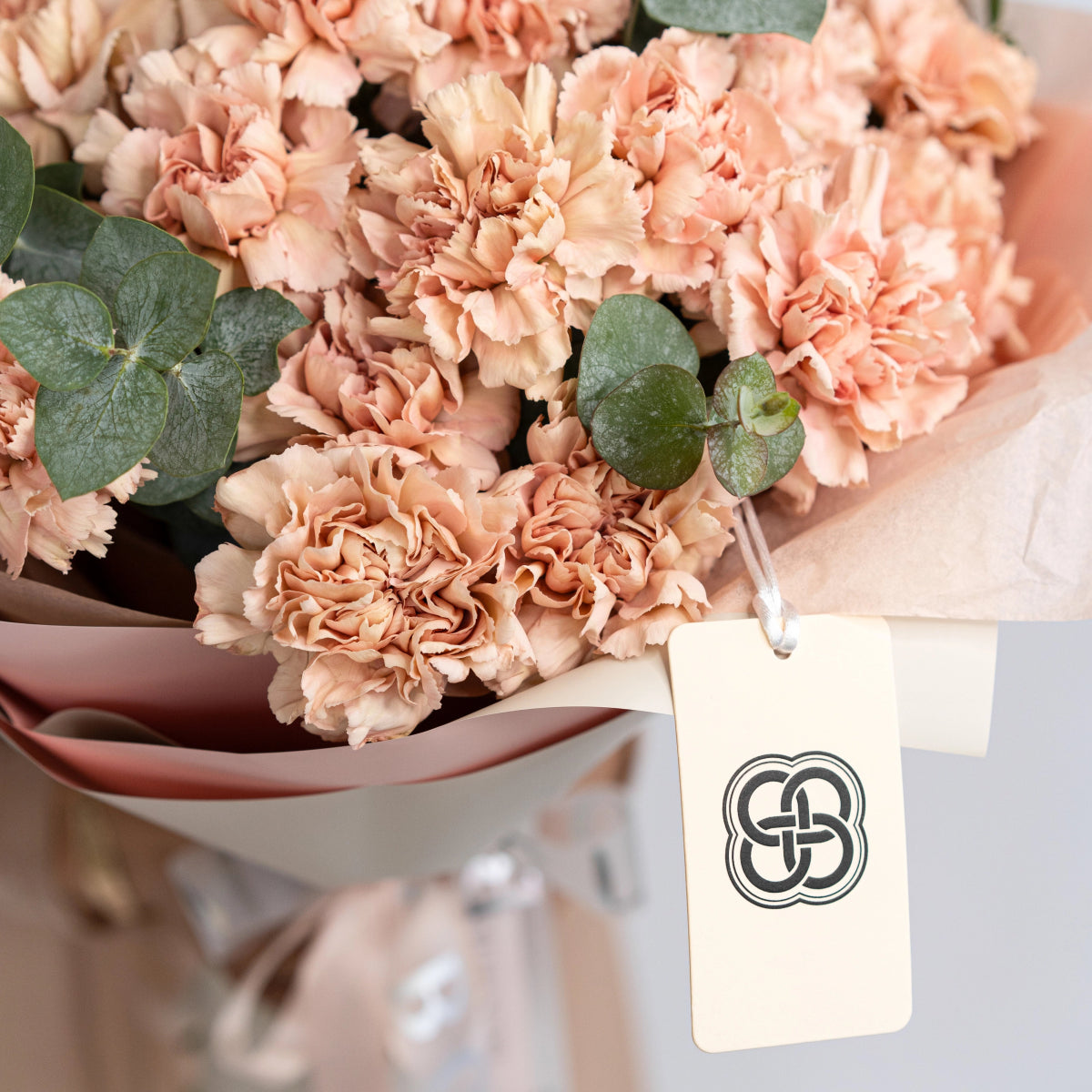 Peach carnation bouquet with green eucalyptus leaves wrapped in brown paper with decorative brand tag