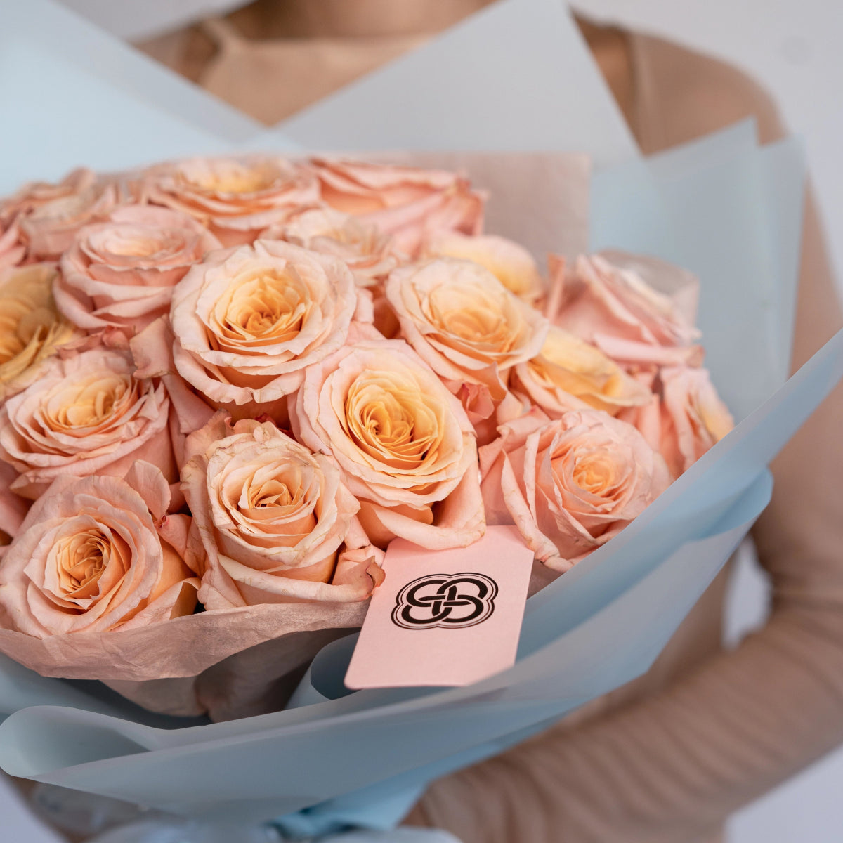 Peach champagne roses bouquet wrapped in white paper with brand tag, luxury flower arrangement gift