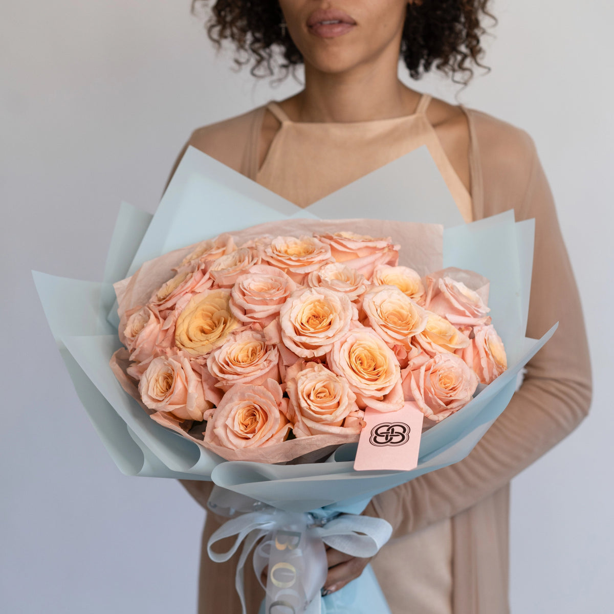 Luxury bouquet of 25 peach and coral roses wrapped in light blue paper with satin ribbon