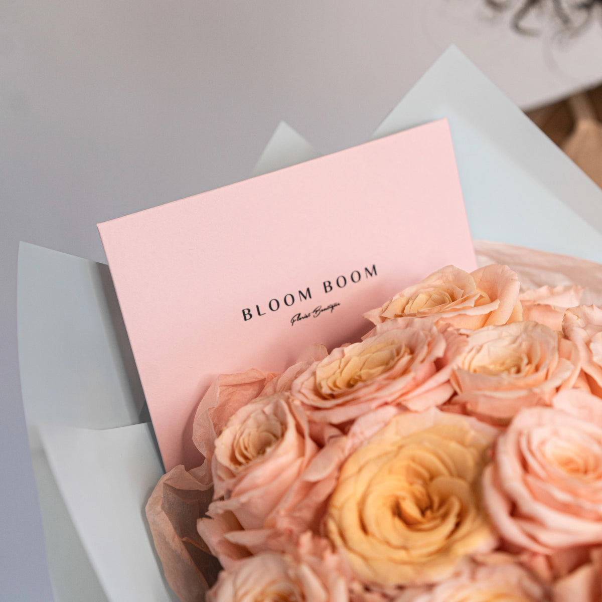 Peach roses bouquet in white wrapping with pink Bloom Boom card, elegant flower arrangement gift