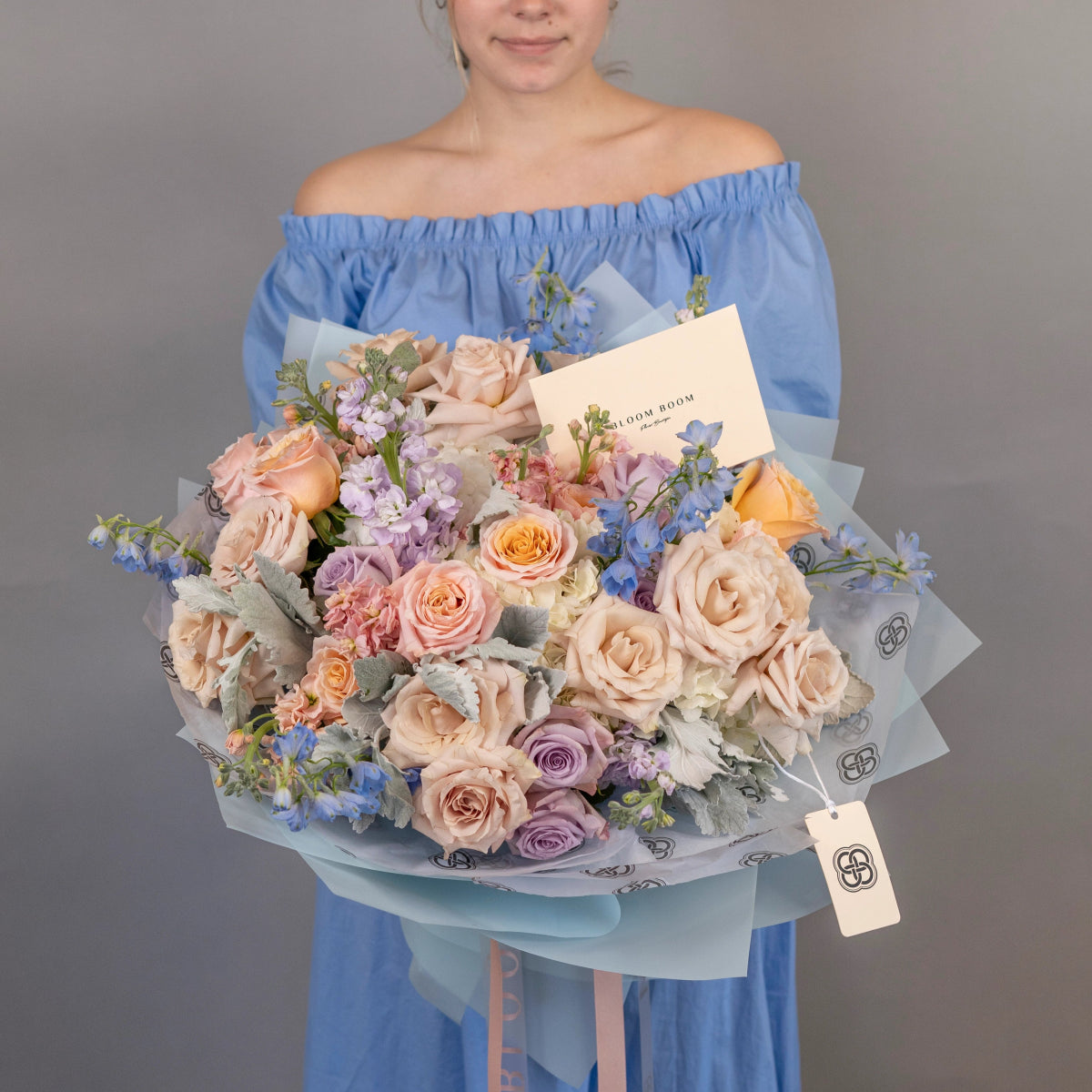 Mixed flower bouquet with peach roses, purple blooms, blue delphinium in light blue wrapping paper