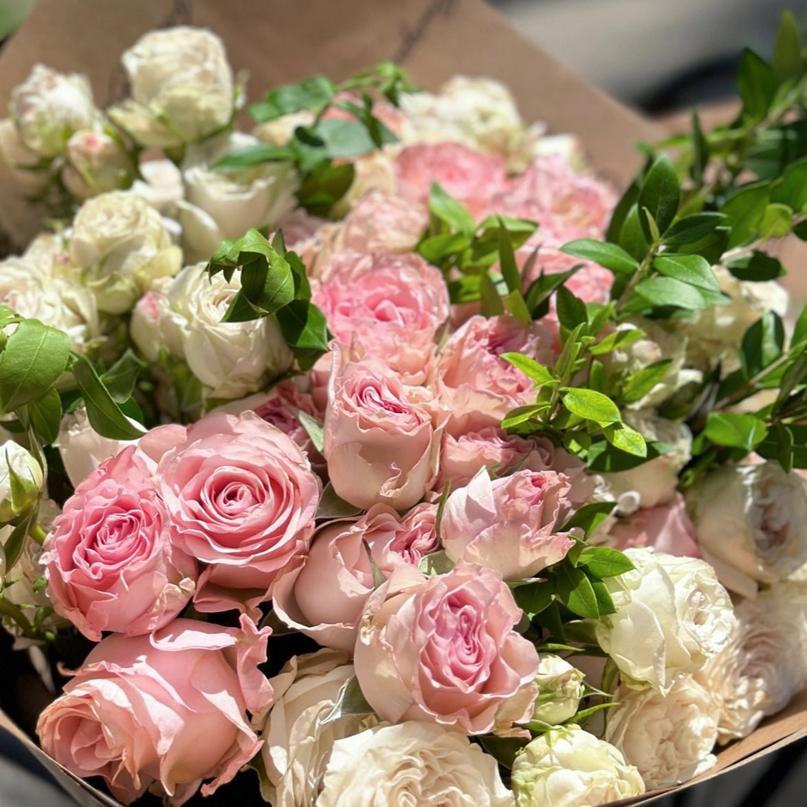 Mixed bouquet of pink and cream roses with green foliage in brown paper wrapping