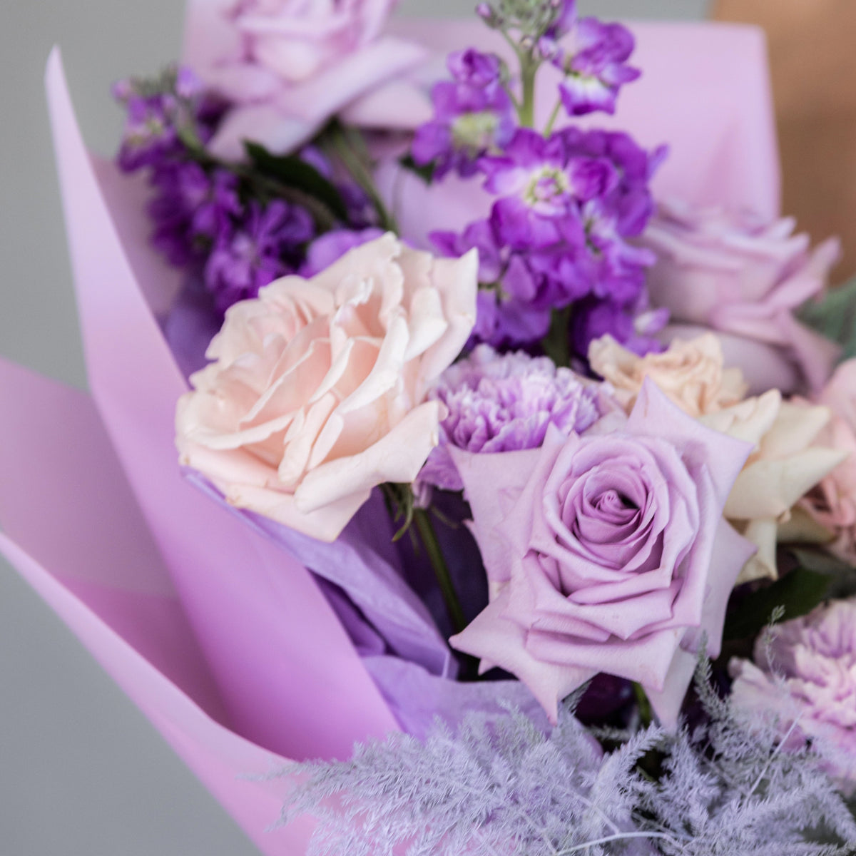 Pink and lavender roses with purple stock flowers wrapped in lilac paper bouquet