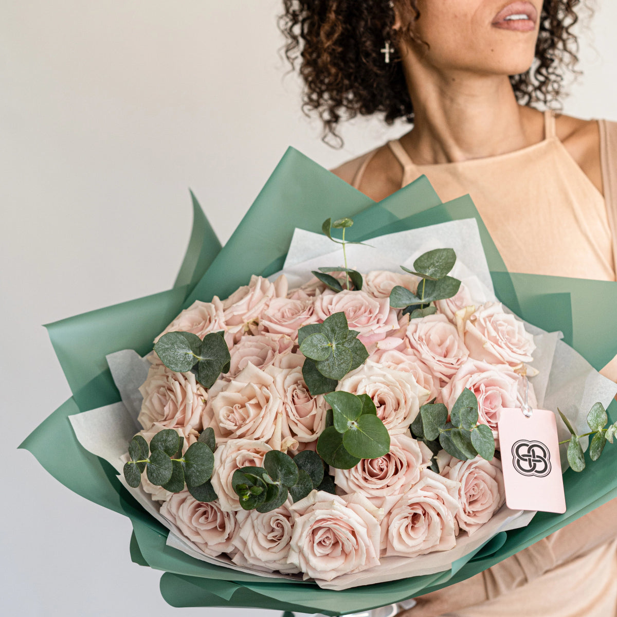 Pink rose bouquet with eucalyptus leaves wrapped in sage green and white paper with brand tag